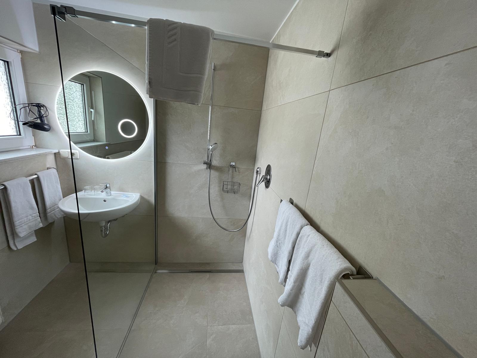 Modernes Badezimmer im Landhaus Schend mit ebenerdiger Walk-in-Dusche und beleuchtetem LED-Rundspiegel
