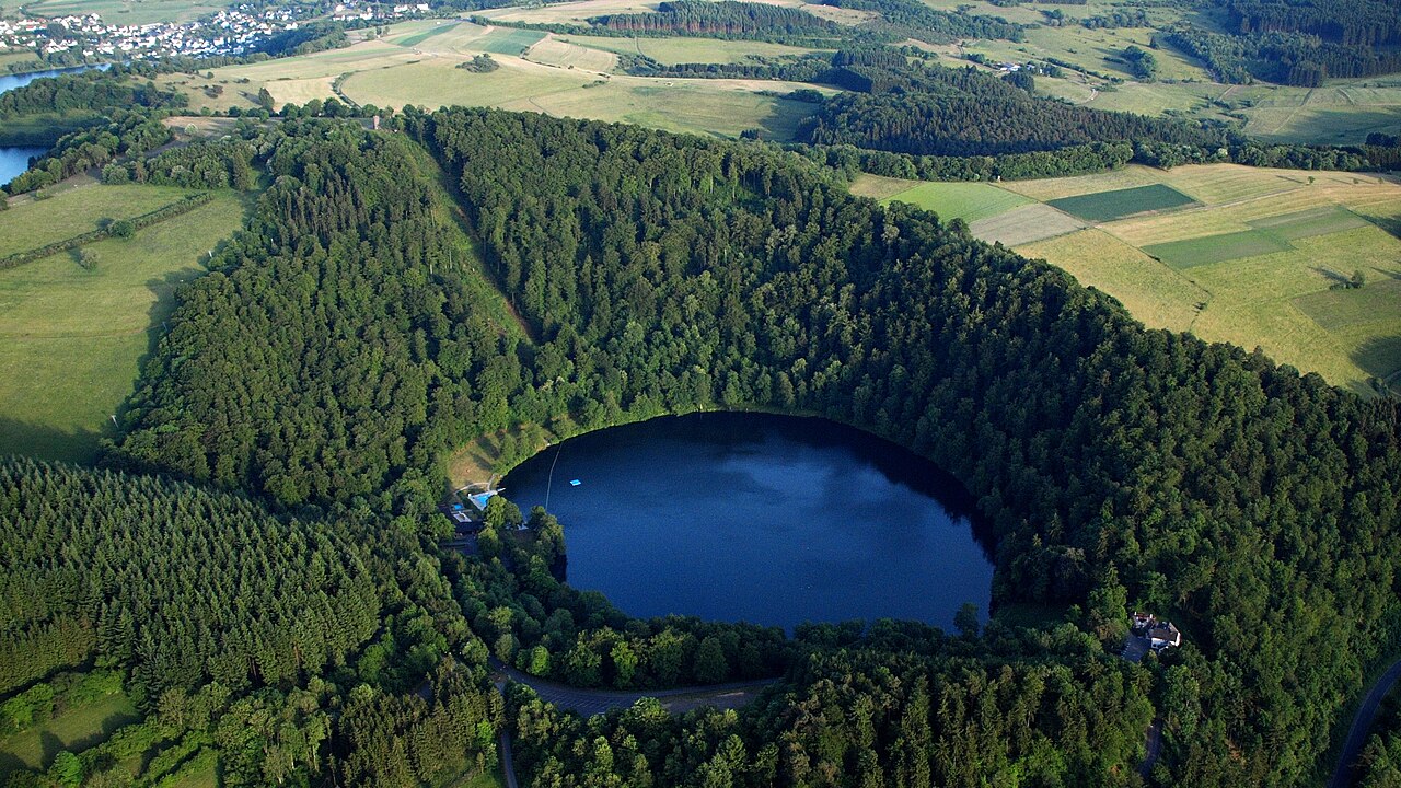 Luftbild des Gemündener Maars bei Daun: ein kreisrunder See in einem bewaldeten Explosionstrichter